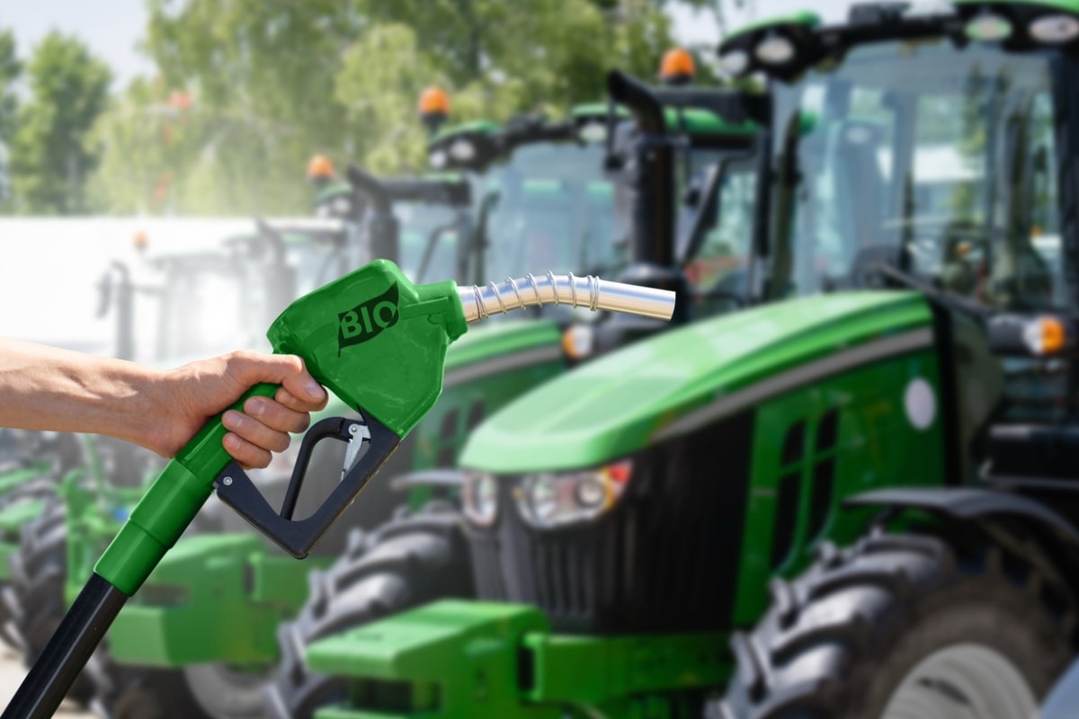 Hand with biofuel refueling nozzle on a background of agricultural tractors.