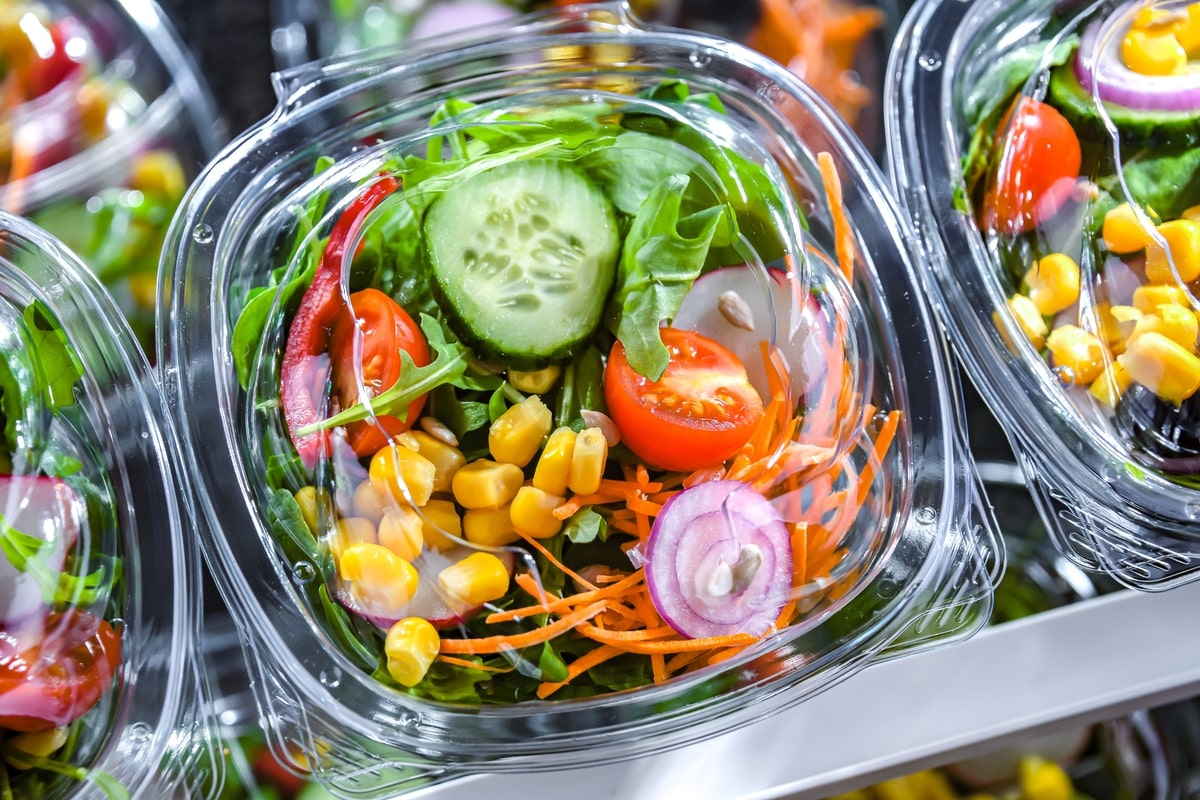 Plastic boxes with pre-packaged vegetable salads, put up for sale in a commercial refrigerator
