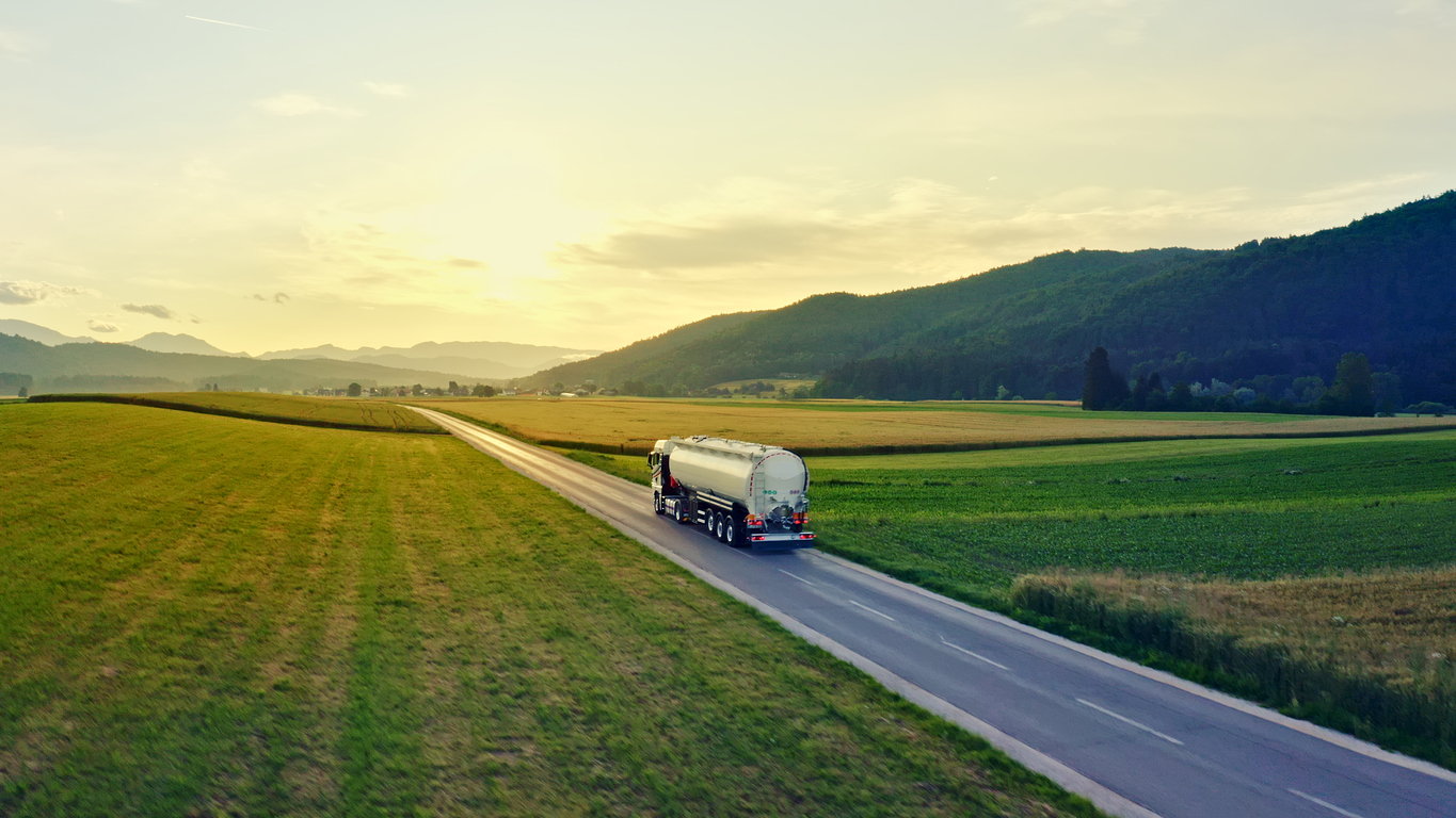 Aerial view of a tanker truck driving down a rural road, surrounded by vast fields and hills